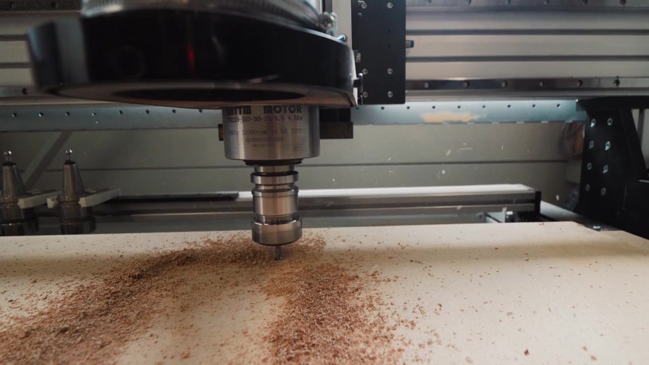 Slowmotion push-in. Vista dal basso di una fresatrice CNC su un foglio di compensato con contorni appena tagliati in un laboratorio di falegnameria