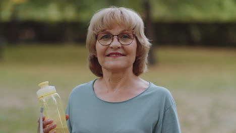 portrait of cheerful senior woman with water bottle outdoors