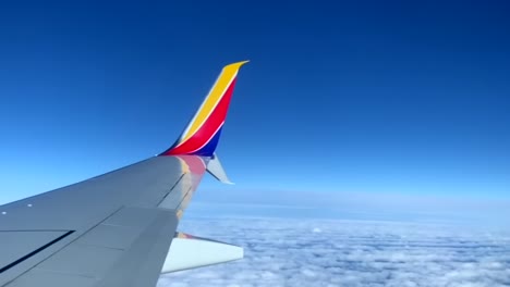 view out airplane window, southwest plane wing above clouds on a clear day