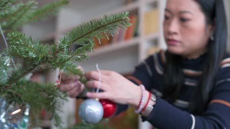 after the holidays, an asian woman is taking ornaments off the tree