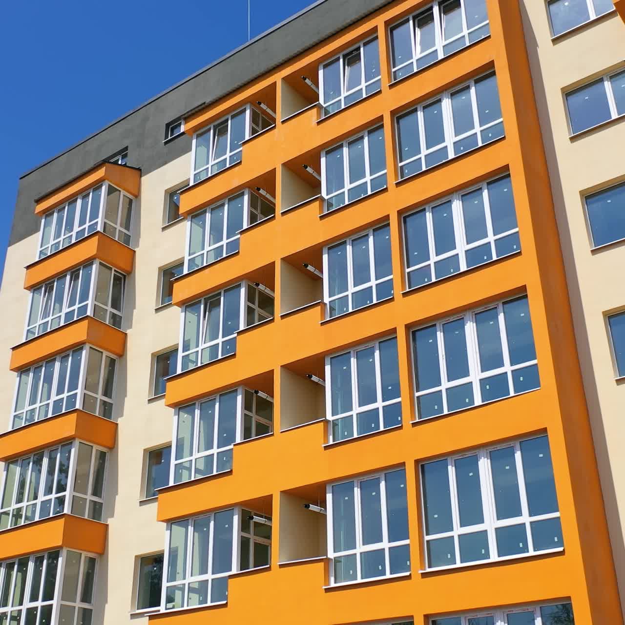 Beautiful high-rise building. Modern block of flats with large balconies on blue sky background in summer. Apartment building of colorful walls. Camera moves down