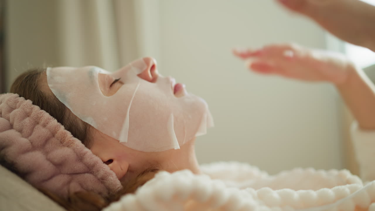 닫힌 눈을 가진 여성은 영양을 주는 얼굴 마스크에서 열을 느다; 평온한 감정을 가진 여성은 얼굴 앞에서 공기를 가속화하여 마스크를 냉각시킨다.