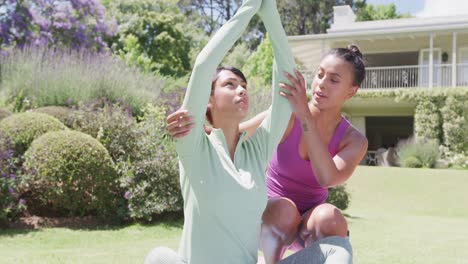 Happy-biracial-sisters-doing-yoga-and-meditating-in-garden,-in-slow-motion