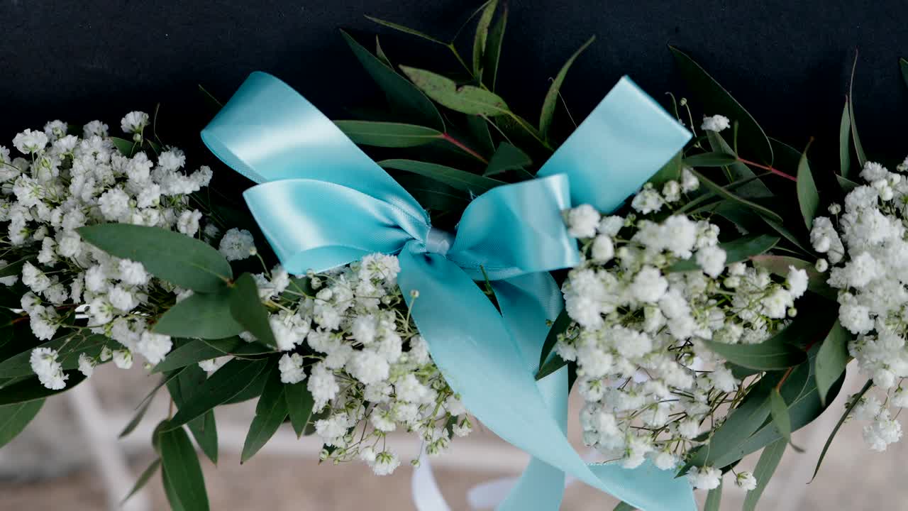 close up of white baby's breath bouquet with blue ribbon and green leaves floral decor