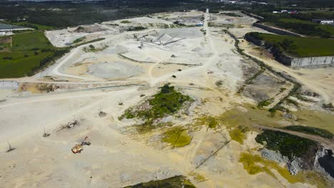 aerial drone footage flying over a large sunny limestone quarry mine that has large conveyor belts with chains and heavy machines and equipment below in the pit that has yellow puddles of waste water