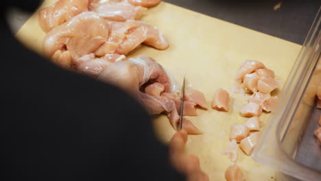 chef cuts chicken breast into bite sized pieces, restaurant kitchen prep of dicing chicken on cutting board, slow motion close up 4k