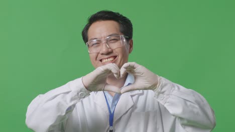 close up of asian man scientist smiling and showing shape heart with hands while standing on the green screen background in the laboratory