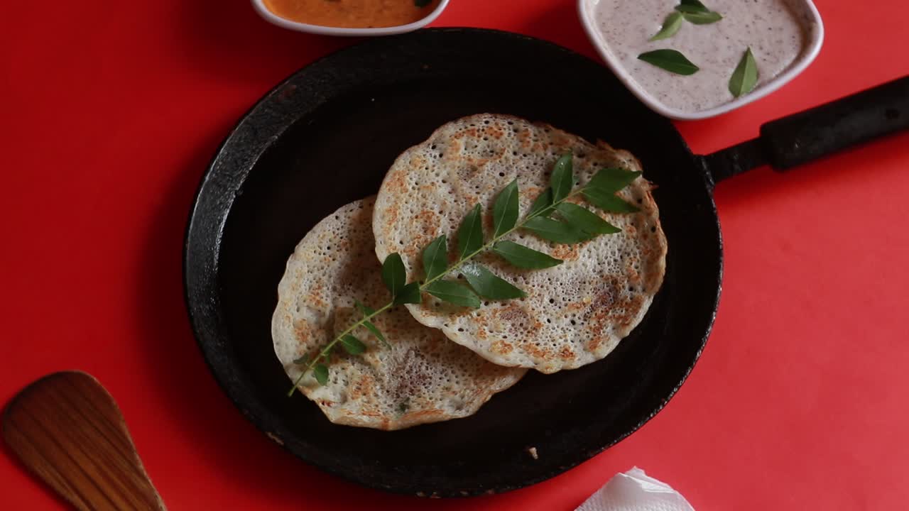 oothappam giratorio - dosa - desayuno del sur de la india con lentejas de arroz y verduras servidas con chutney de coco aislado sobre fondo rojo