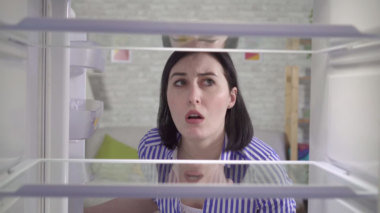 젊은 여성이 빈 냉장고를 들여다보고