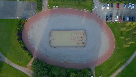 Soccer-practice-drills-in-a-small-soccer-cage-ina-park,-wide-top-shot-with-camera-descending