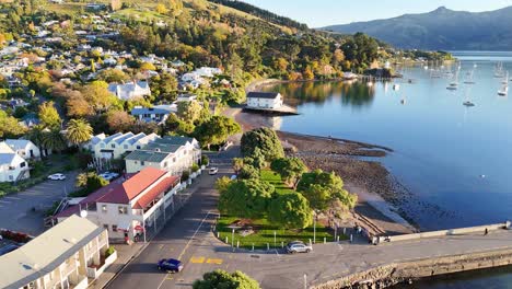 drone footage captures akaroa's serene harbor, showcasing boats, hills, and vibrant sunset reflections over calm waters