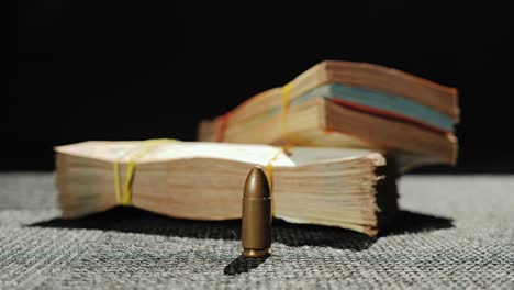 close up of bullet and rubber-banded banknotes on fabric surface with hard light