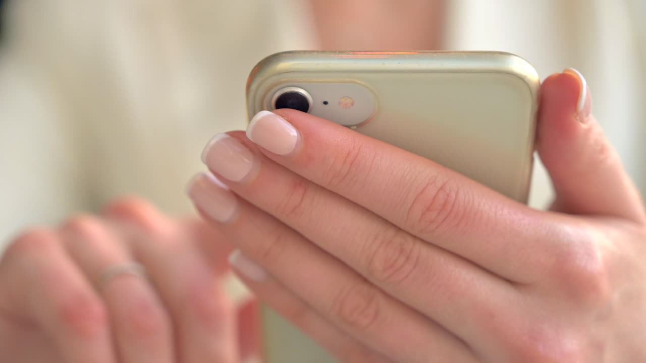 Primo piano di una donna con un blazer bianco che scorre qualcosa sul telefono a un tavolo di un ristorante