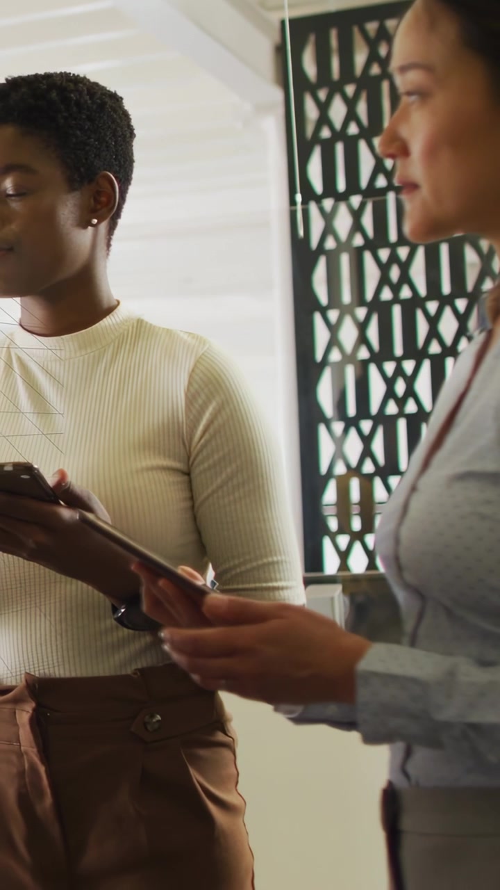 Vertical video: Two women hearing speaker tapping tablets reviewing business data as charts forming