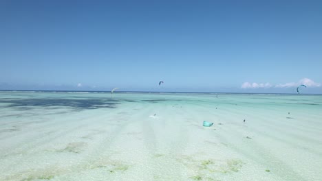 kiteboarders surf over tropical beach shoals on bright, sunny day