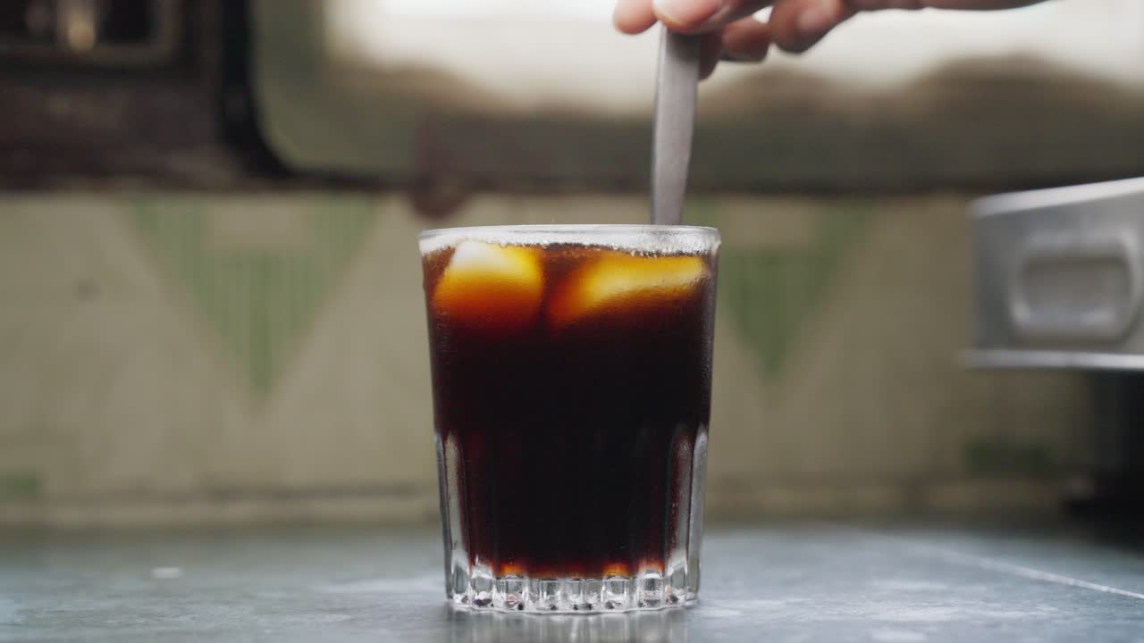 A close-up footage of stirring the ice cubes in an iced tea glass with a small stainless knife