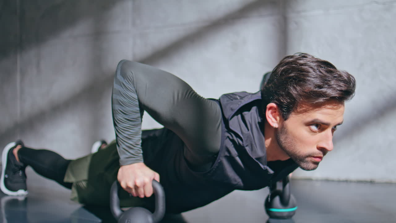 Muscular sportsman making push ups in plank using kettlebells in studio closeup