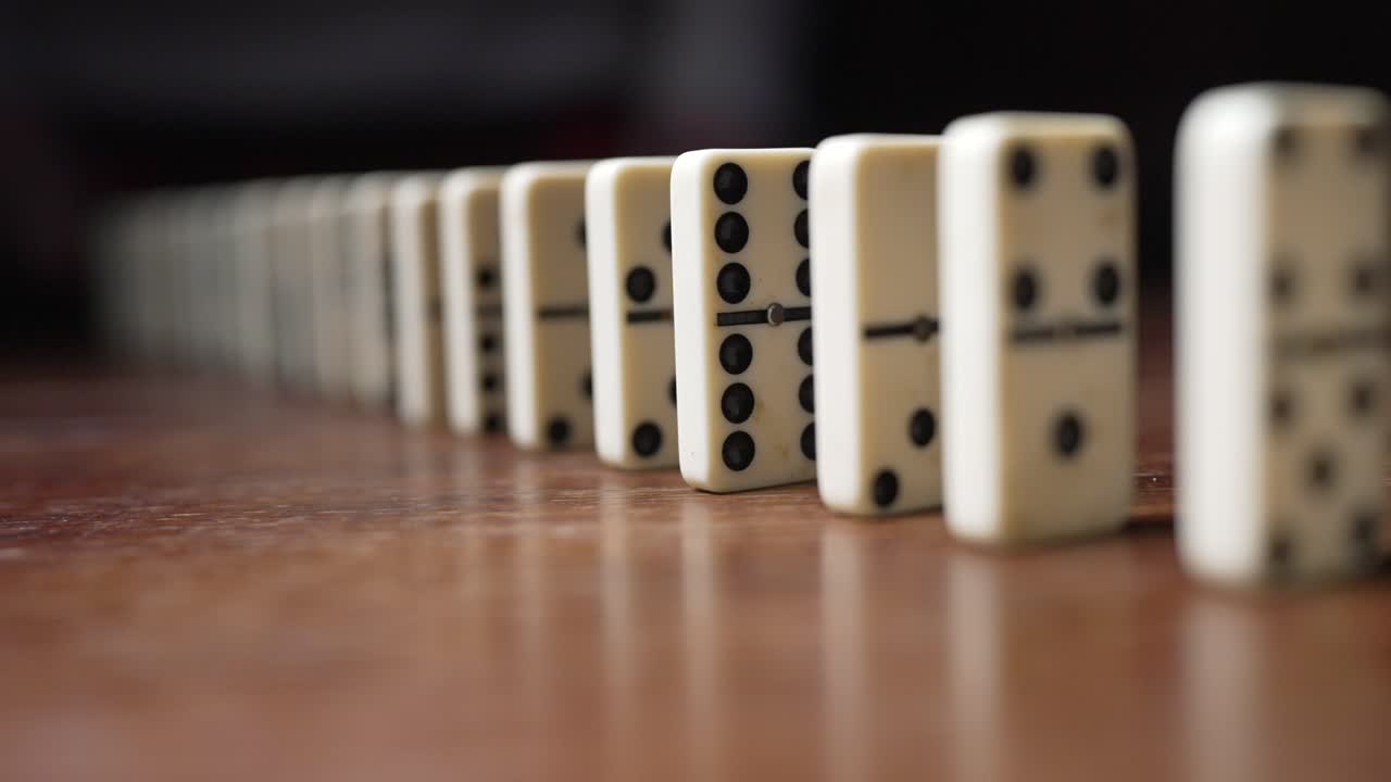 A silhouette pushes a line of white dominos, triggering a slow-motion chain reaction and showcasing the domino effect