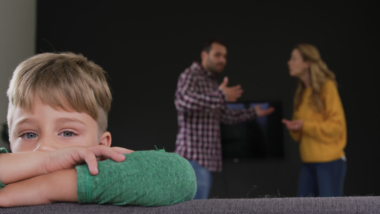 Ragazzo appoggiato al divano mentre i genitori litigano sullo sfondo a casa, 4K
