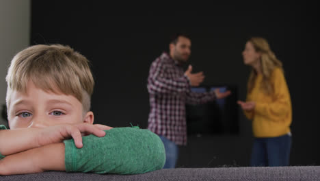 boy leaning on sofa while parents arguing in background at home 4k