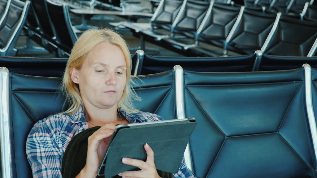 una mujer usa una tableta en un salón del aeropuerto mientras espera un vuelo