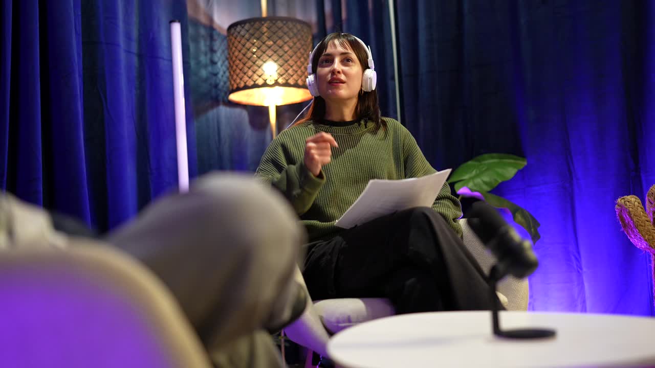 Ung kvinde med hovedtelefoner, der taler og gestikulerer i et podcaststudie