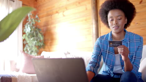 happy african american woman using laptop and credit card in living room, in slow motion