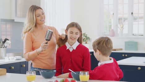 Mutter-Bürstet-Ihrer-Tochter-Die-Haare,-Während-Kinder-In-Schuluniform-Zu-Hause-Frühstücken