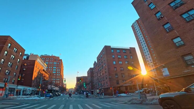 New York, USA, 5 dicembre 2025: Strada con palazzi di appartamenti in mattoni a New York all'alba. Veicoli percorrono una strada asfaltata costeggiata da strutture residenziali sotto un cielo sereno
