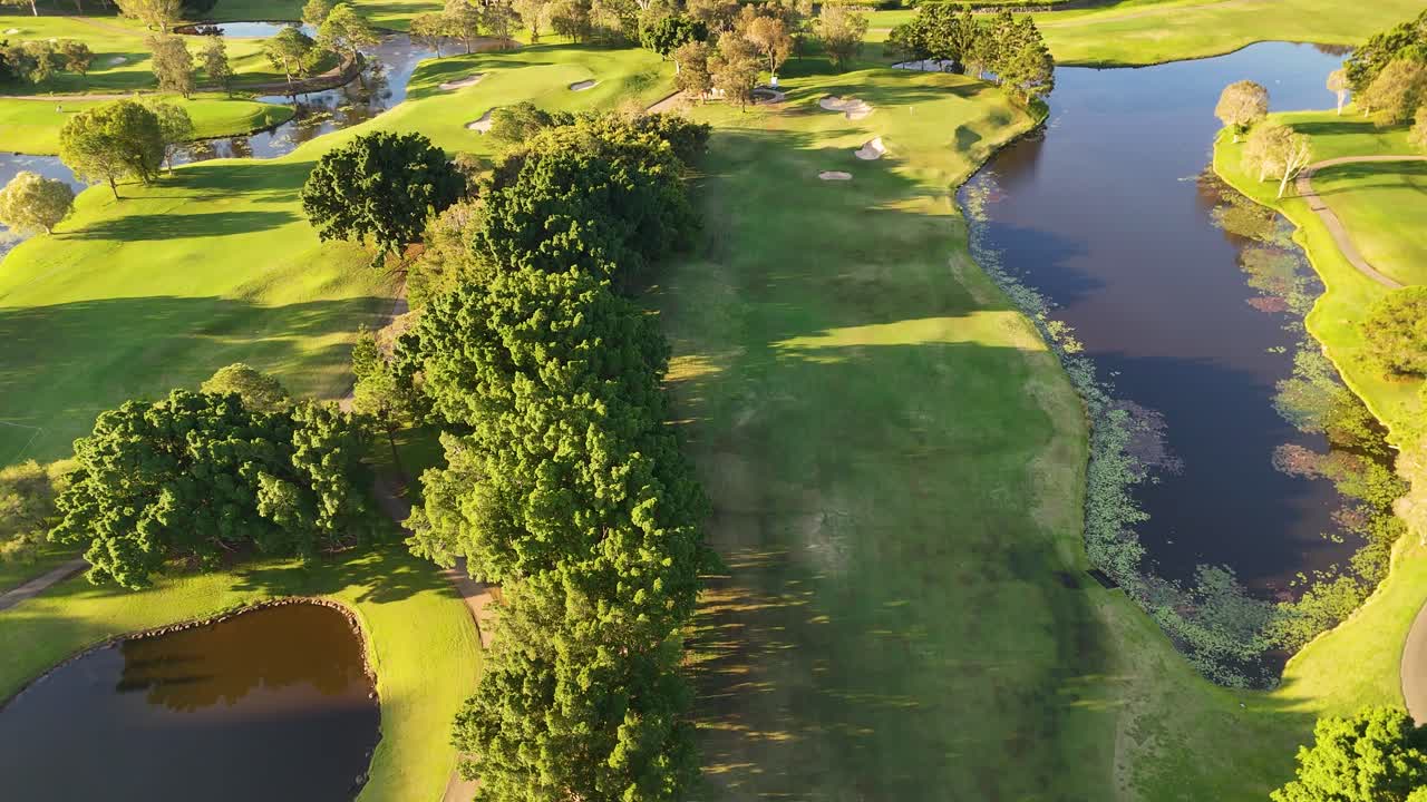 Drone footage captures a serene golf course landscape with lush greenery and water features during golden hour