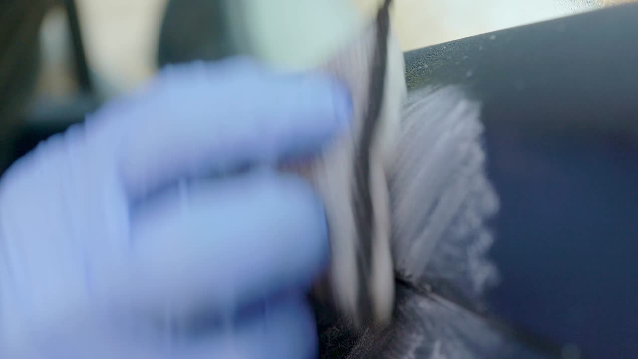 Cleaning car interior leather door car with microfibre scrub pad and wearing blue nitrile gloves