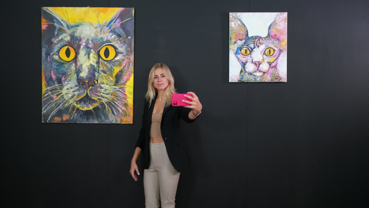 예술 갤러리에서 고양이 그림 앞에서 셀피를 찍는 여자