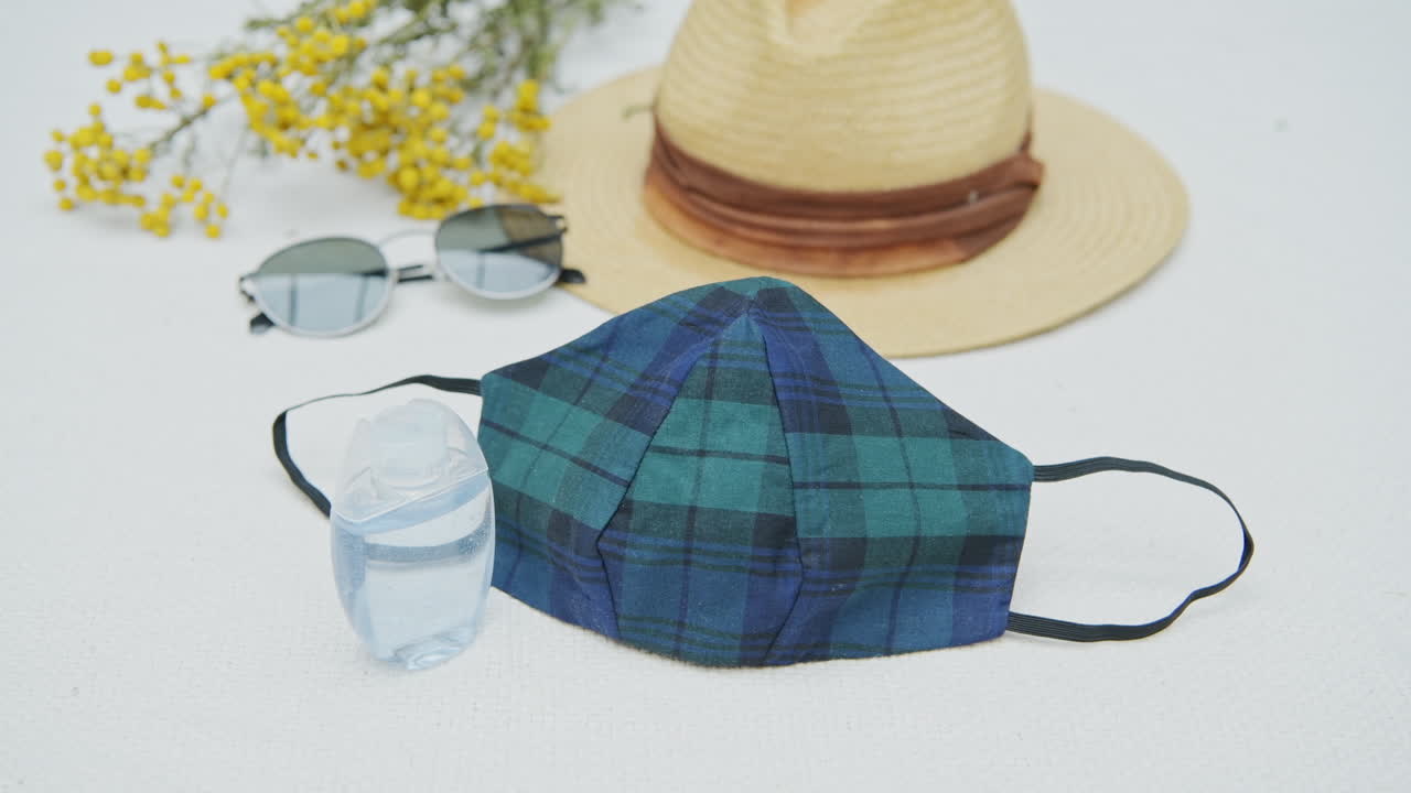 Flat lay of coronavirus travel kit: fashion mask, hand sanitizer, sunglasses and hat