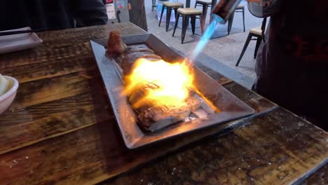 el chef usa una antorcha para cocinar pescado en una mesa de madera.