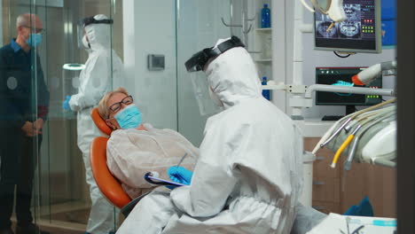 dentist nurse in protective suit taking notes on clipboard