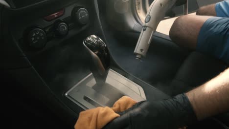 Hombre-Con-Guantes-Negros-Limpiando-El-área-De-La-Palanca-De-Cambios-Del-Coche-Con-Vapor