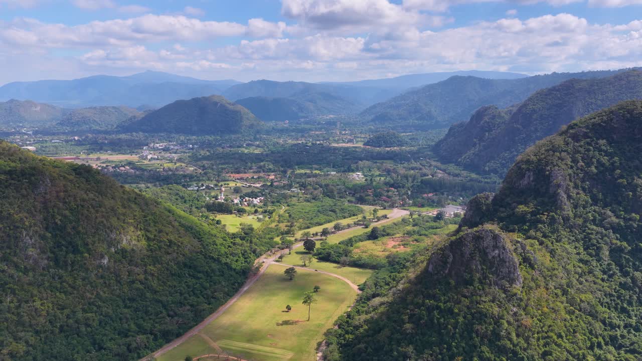 Filmagem com drone captura um campo de golfe verde aninhado entre montanhas tropicais sob um céu claro