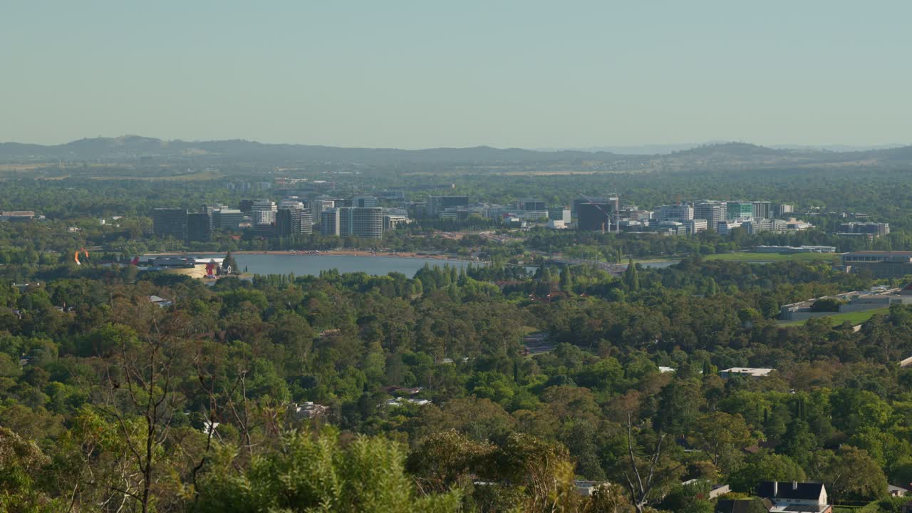 A morning cityscape of Canberra’s CBD, featuring construction cranes and vehicles moving across the bridge over Lake Burley Griffin, highlighting urban growth.