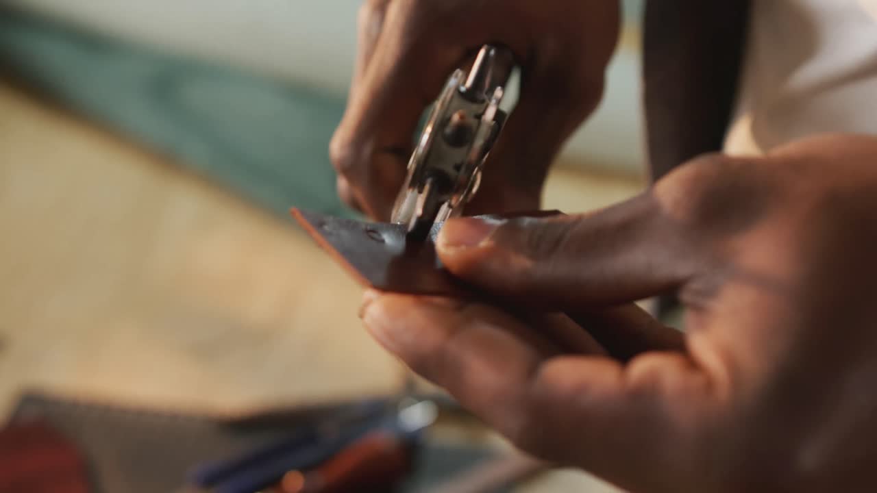 Hands of african american craftsman using tools to make a hole in leather workshop