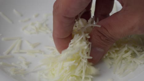 hand reaches for a small pile of shredded cheese on a white plate for cooking or topping.