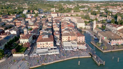 antena dando vueltas sobre lazise en el lago garda , paseo con turistas y construcciones de la ciudad en el fondo