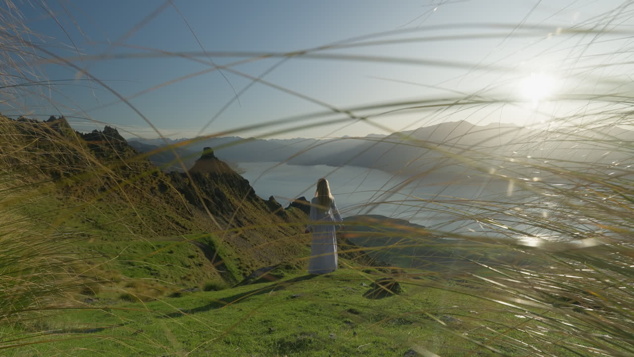 элегантная модель в белой траве в альпийских горах с травой на переднем плане и ярким солнечным светом