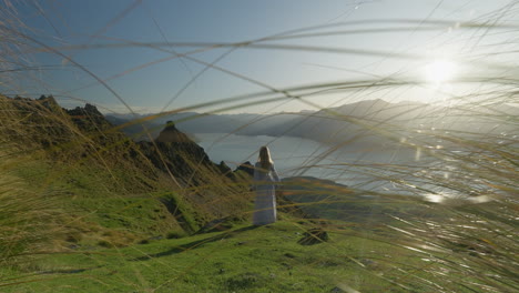 elegant model in white grass in alpine mountains with grass in foreground and bright sunlight