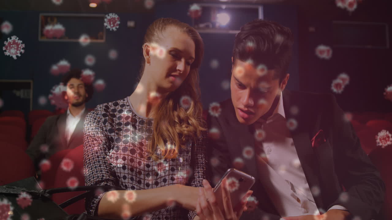 células de covid-19 contra una pareja que usa un teléfono inteligente en el teatro