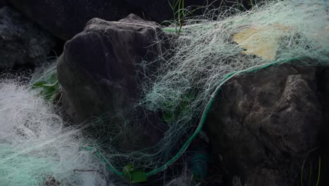 Close-up-of-commercial-fishing-net-abandoned-as-trash-on-ocean-side-rocks