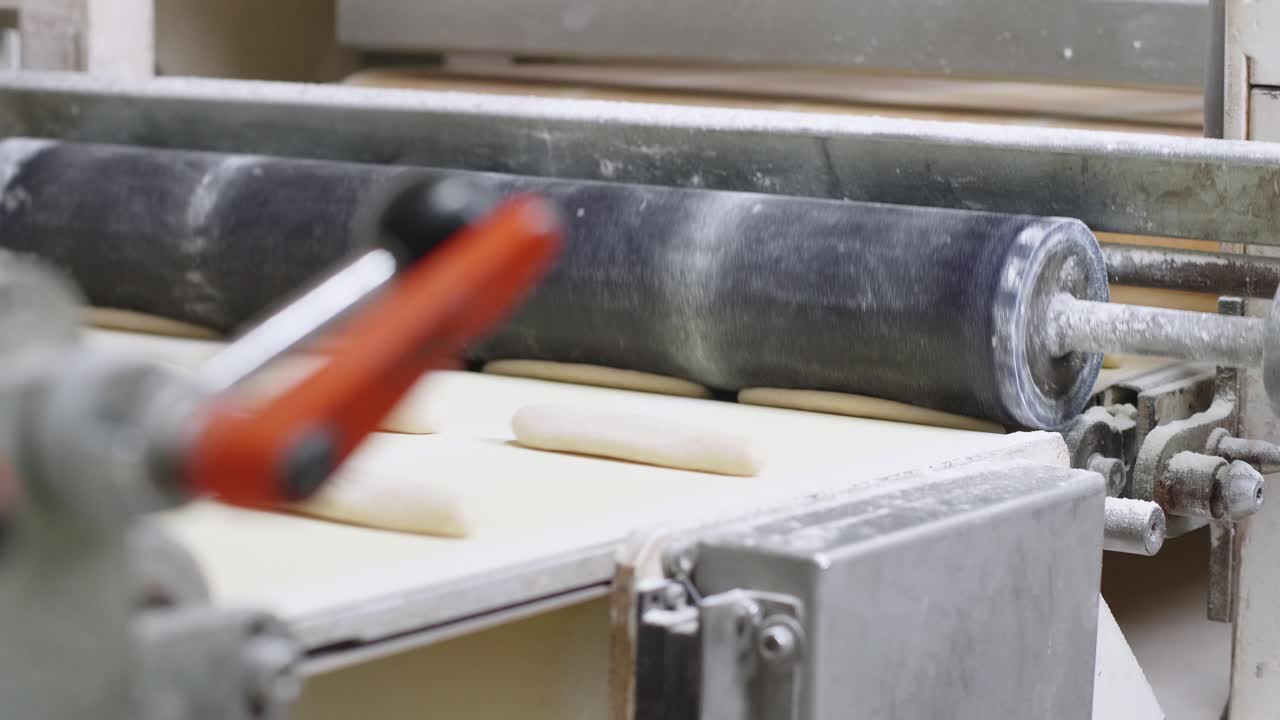 Close Up View Of Fresh Bread Dough Rolls Moving On Conveyor Belt And Being Pressed By Roller