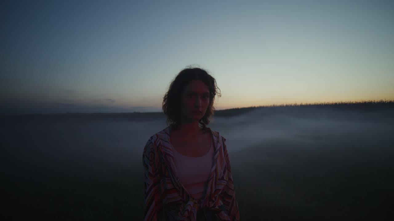mujer en un campo al atardecer, envuelta en niebla