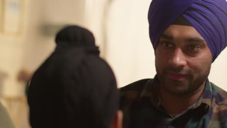 close up of father tying turban onto head of young sikh son with top knot sitting on sofa at home 2