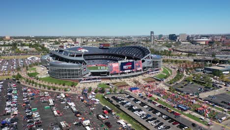 cinematic drone shot revealing empower field at mile high stadium exterior with cars parked in parking spaces, main street highway with downtown denver city view backdrop, colorado