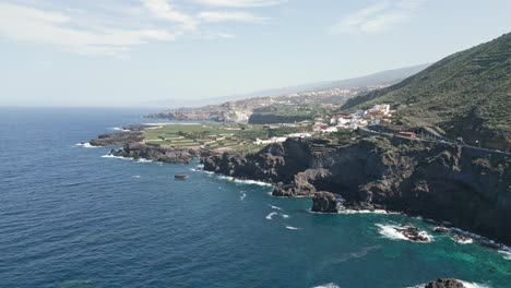 rocky basalt cliffs raise bombarded by strong ocean waves with tenerife in distance